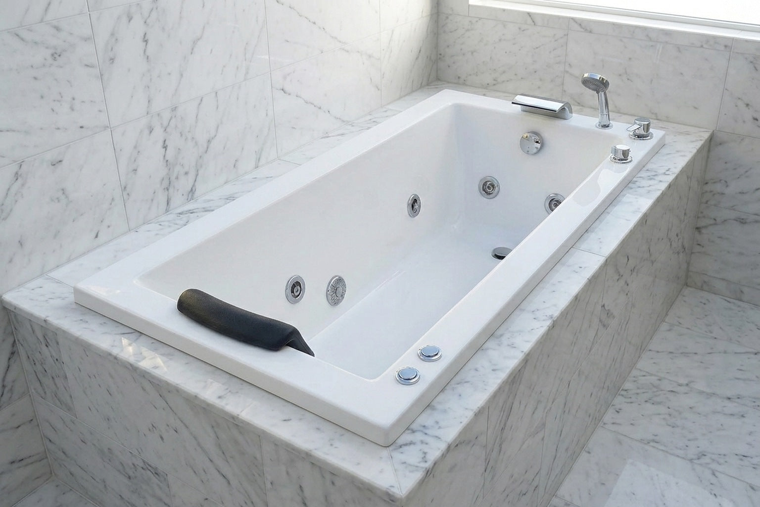 Tina hidromasaje Cube Plus empotrada en baño de mármol, con grifería cascada y almohada